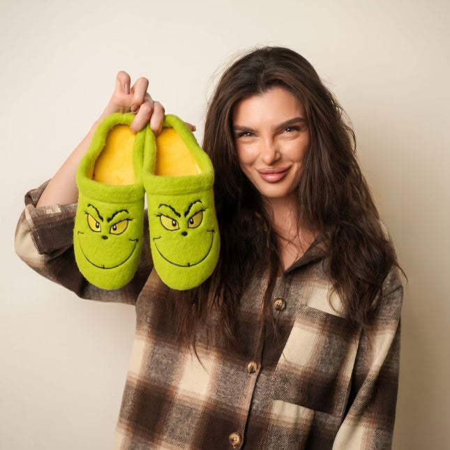 Woman holding a pair of BELSTA The Mischief Wool-Blend Slippers — green mules with embroidered grumpy face