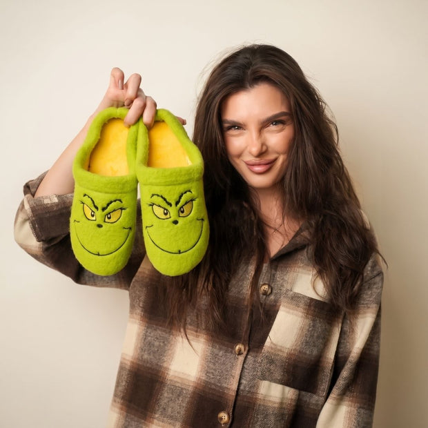 Woman holding a pair of BELSTA The Mischief Wool-Blend Slippers — green mules with embroidered grumpy face
