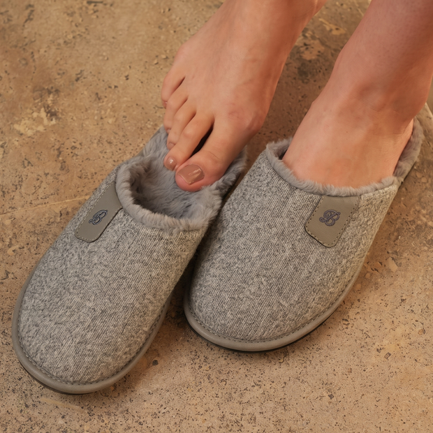 Woman stepping into BELSTA The Pebble Knit Slippers — grey knit mules with faux-fur lining, lifestyle shot
